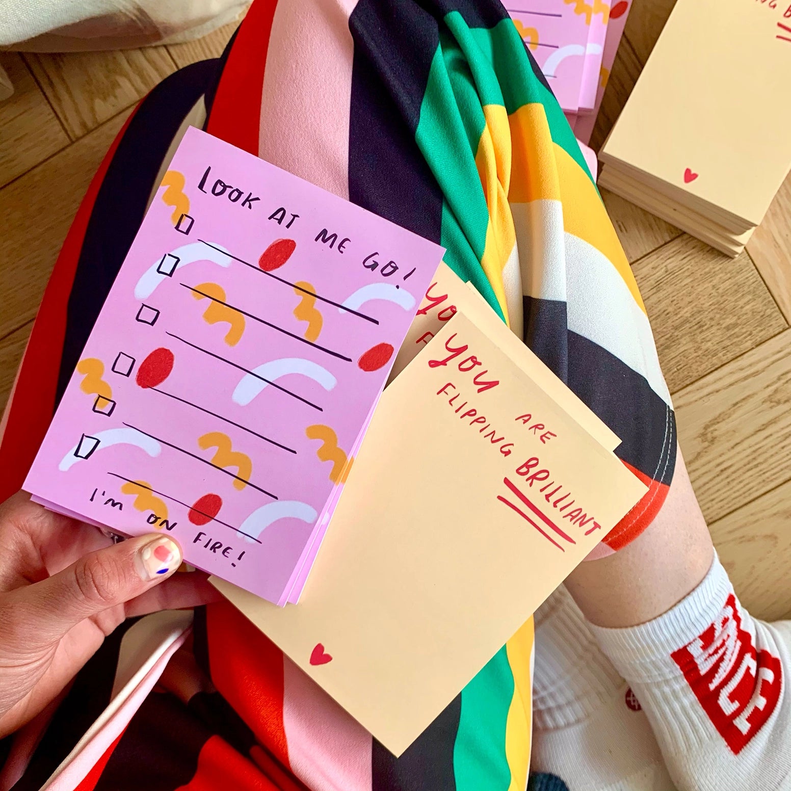 Person holding colorful notepads with motivational messages on a wooden floor.