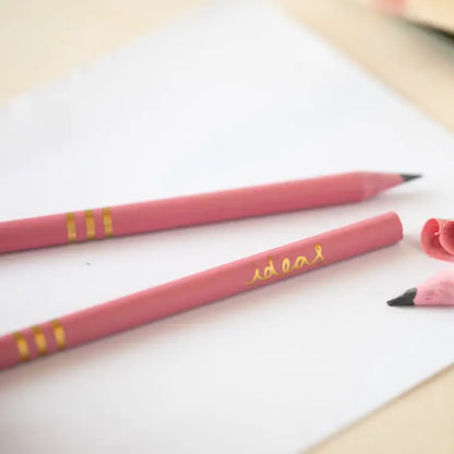 Close up of three dark pink recycled pencils showing the word &