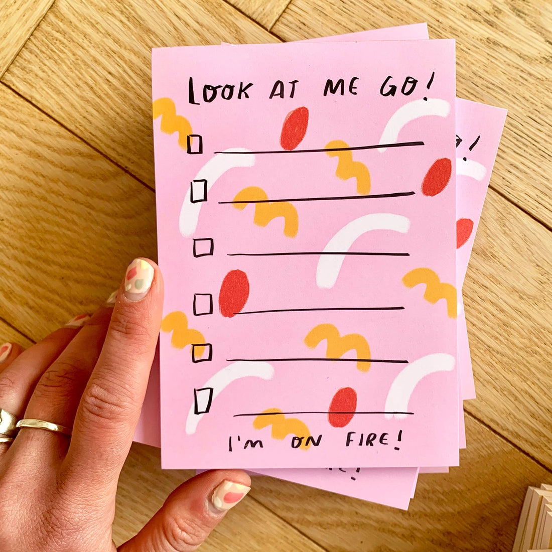 Pink notepad with colorful design and text held by a hand on a wooden surface