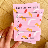 Pink notepad with colorful design and text held by a hand on a wooden surface