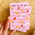 Pink notepad with colorful design and text held by a hand on a wooden surface