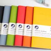 A variety of colourful recycled leather journals fanned out on a white background