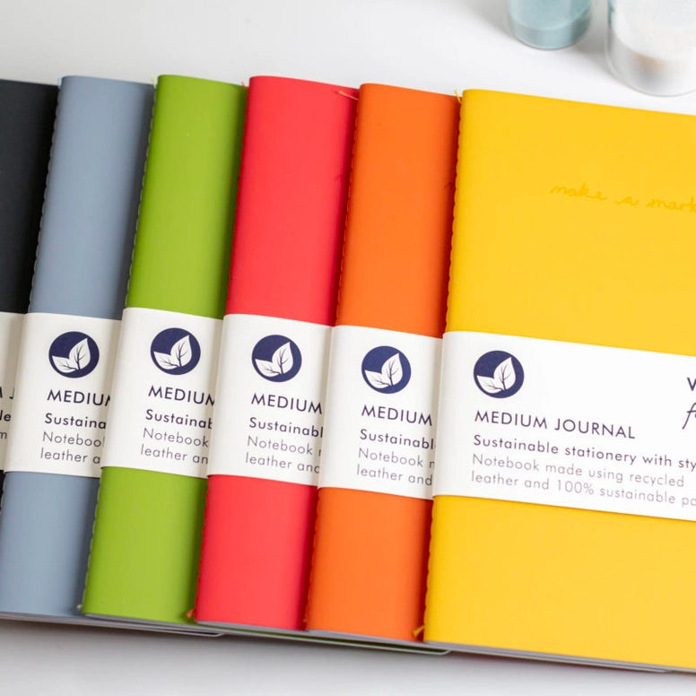 A variety of colourful recycled leather journals fanned out on a white background